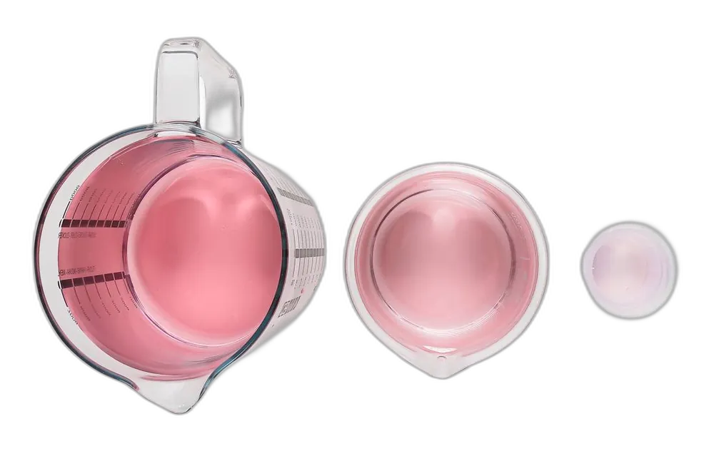 Dasselbe kolloidale Gold in gro&szlig;er Flasche, Messbecher und kleinem Becher &ndash; von kr&auml;ftig rosa bis fast klar